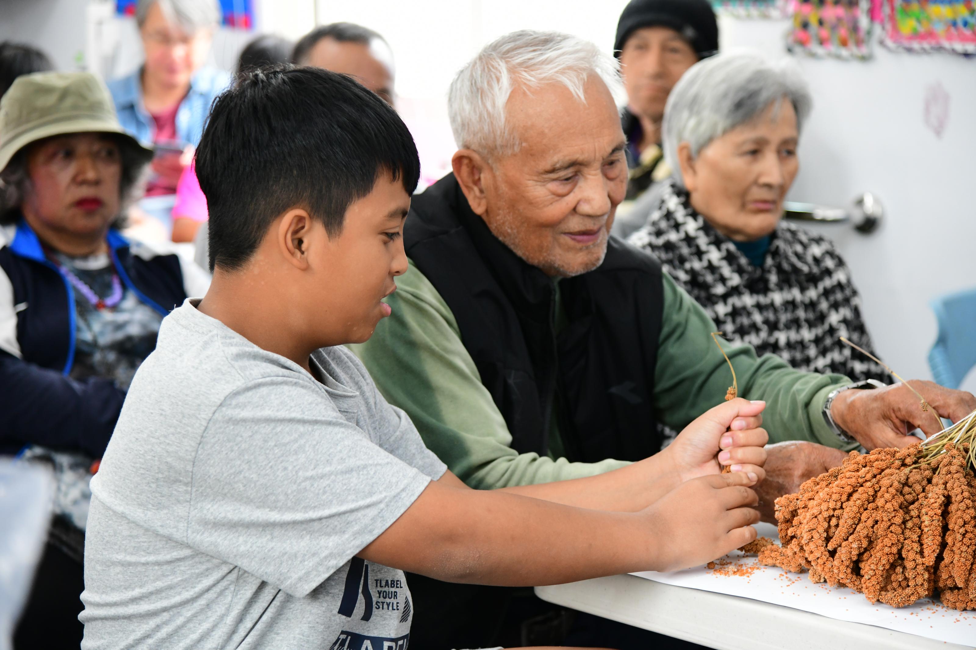 Young students and the elderly learn how to hull millet together.